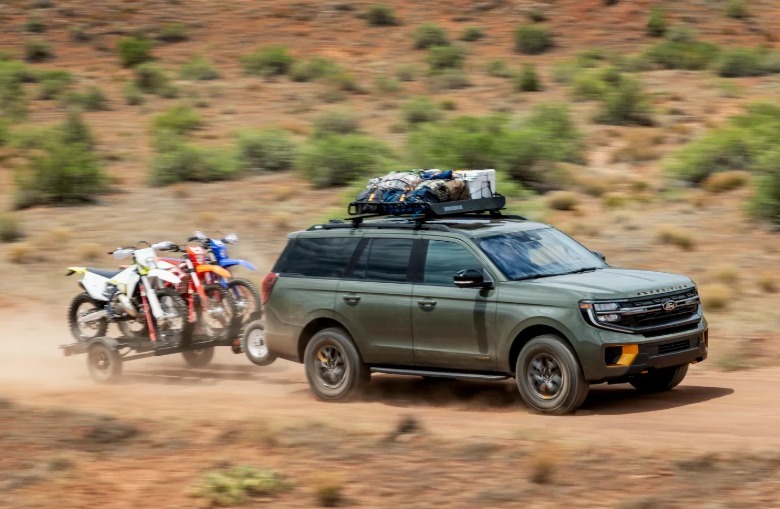 Front 3/4 view of a green Ford Expedition towing dirt bikes.