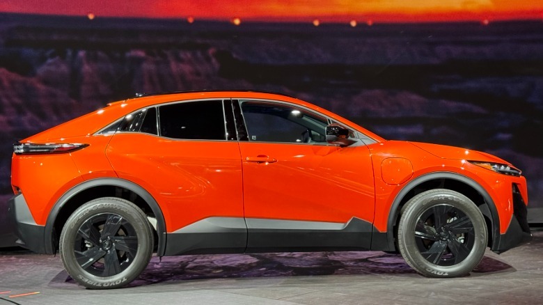 A side view of a bright orange Uncharted parked at the LA Auto Show in front of a screen showing a glimpse of a sunset