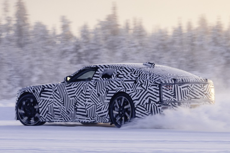 Rear 3/4 view of a camouflaged Jaguar GT prototype drifting in snow