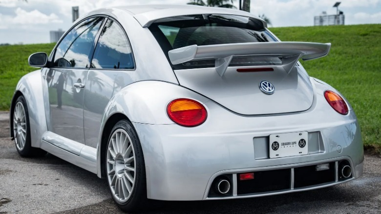 Rear three-quarters shot of the silver Beetle RSi parked on asphalt in front of green grass and a cloudy sky